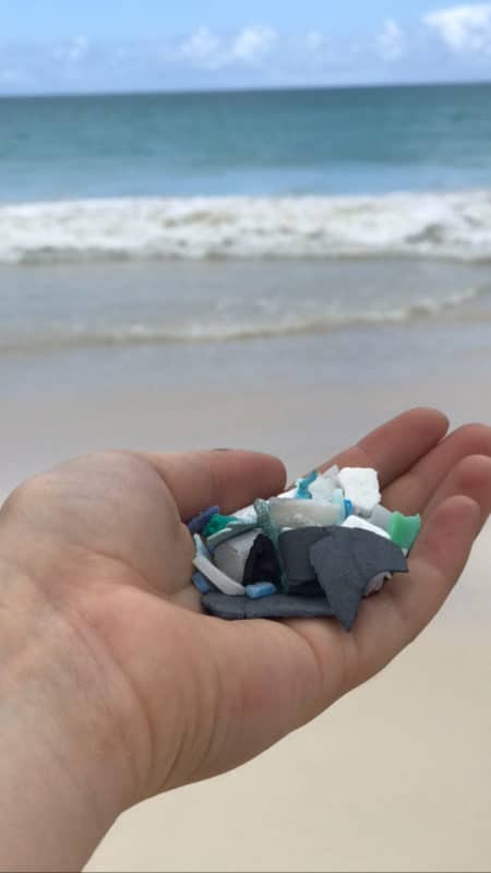 Outstretched hand holds microplastics found during beach cleanup in Oahu